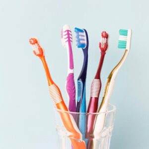 Multi-colored toothbrushes in a glass cup, blue background